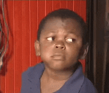 a young boy in a blue shirt is making a funny face while standing in front of a red curtain .