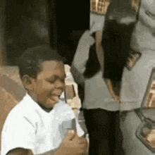 a young boy is eating an ice cream cone in front of a car while a woman stands behind him .