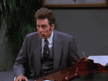 a man in a suit and tie sits at a desk with the words " i don 't even really work here " above him